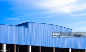 Blue Corrugated metal Roof of large Industrial Warehouse Building against blue sky Background in Perspective side view