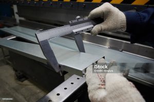 A specialist at the factory measures the accuracy of bending of  metal sheet used as a cover for an industrial radiator of a convector type with vernier caliper, quality control on a production line